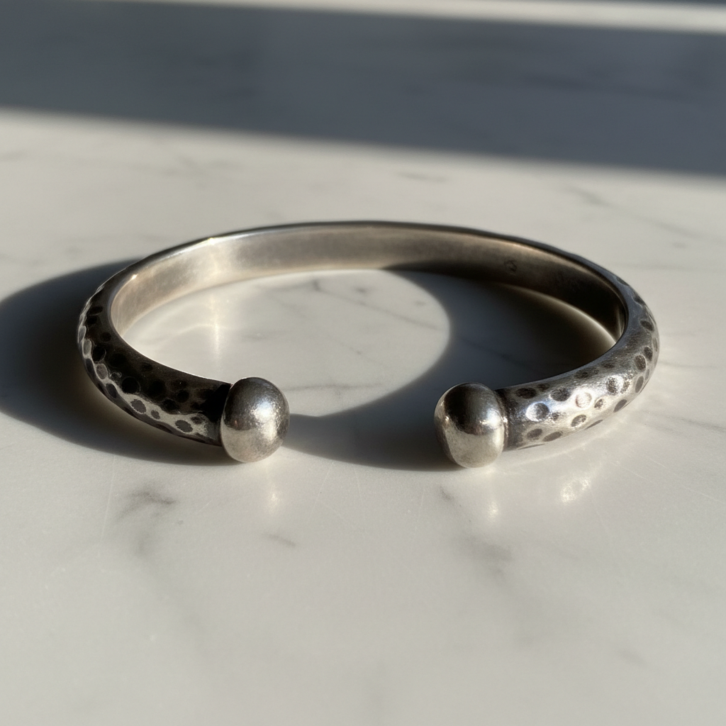 Hammered sterling silver cuff bracelet on white marble surface, bright studio light