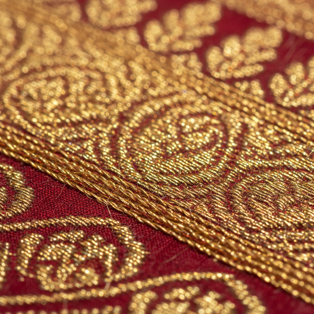 Extreme macro close-up of gold zari border on a Banarasi silk saree, individual threads visible catching studio light